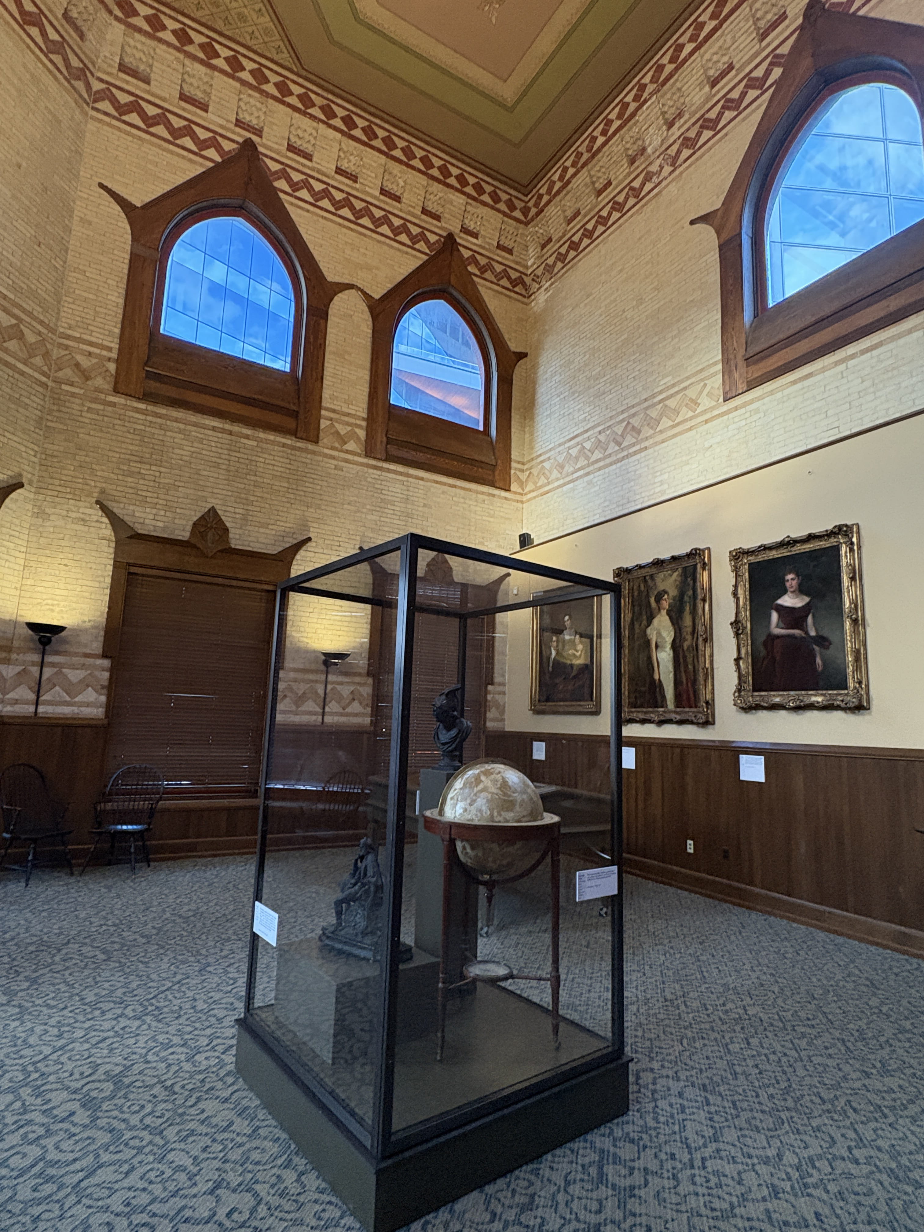 A globe stationed in front of portraits on a wall.
