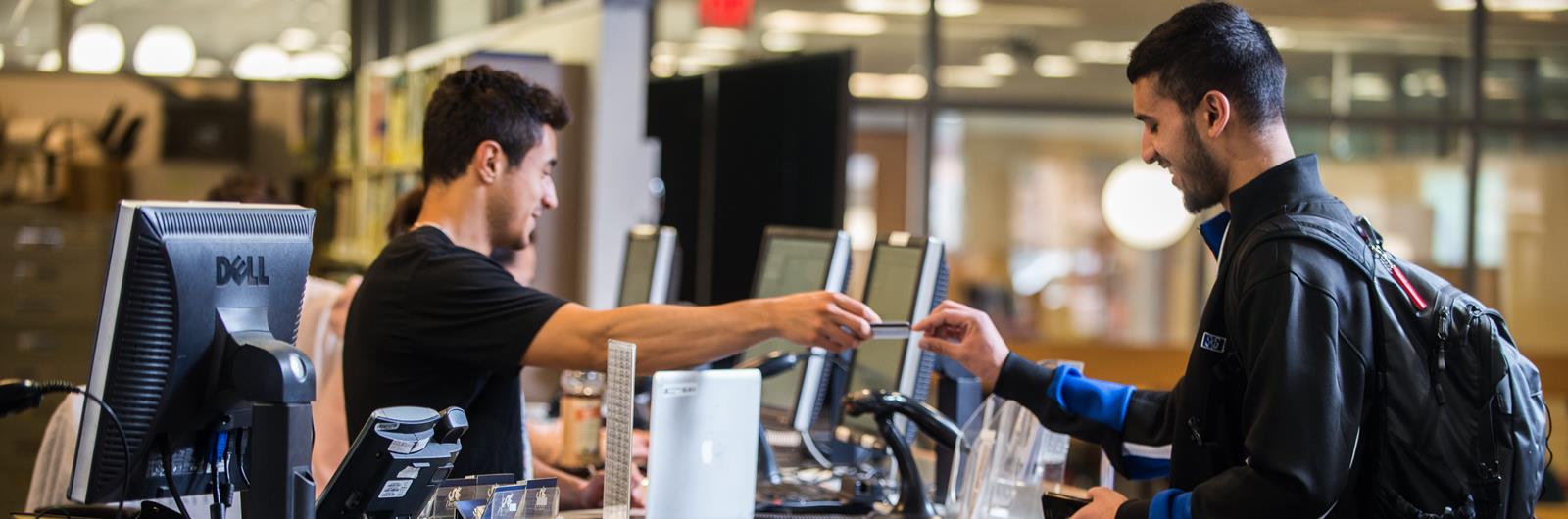 Two people talk at a service desk in a library