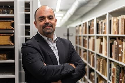 Pedro Raposo smiling with arms crossed in a library stacks.