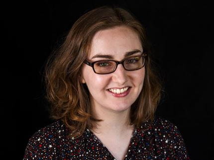 Headshot of Sarah Hughes wearing glasses in front of black backdrop.