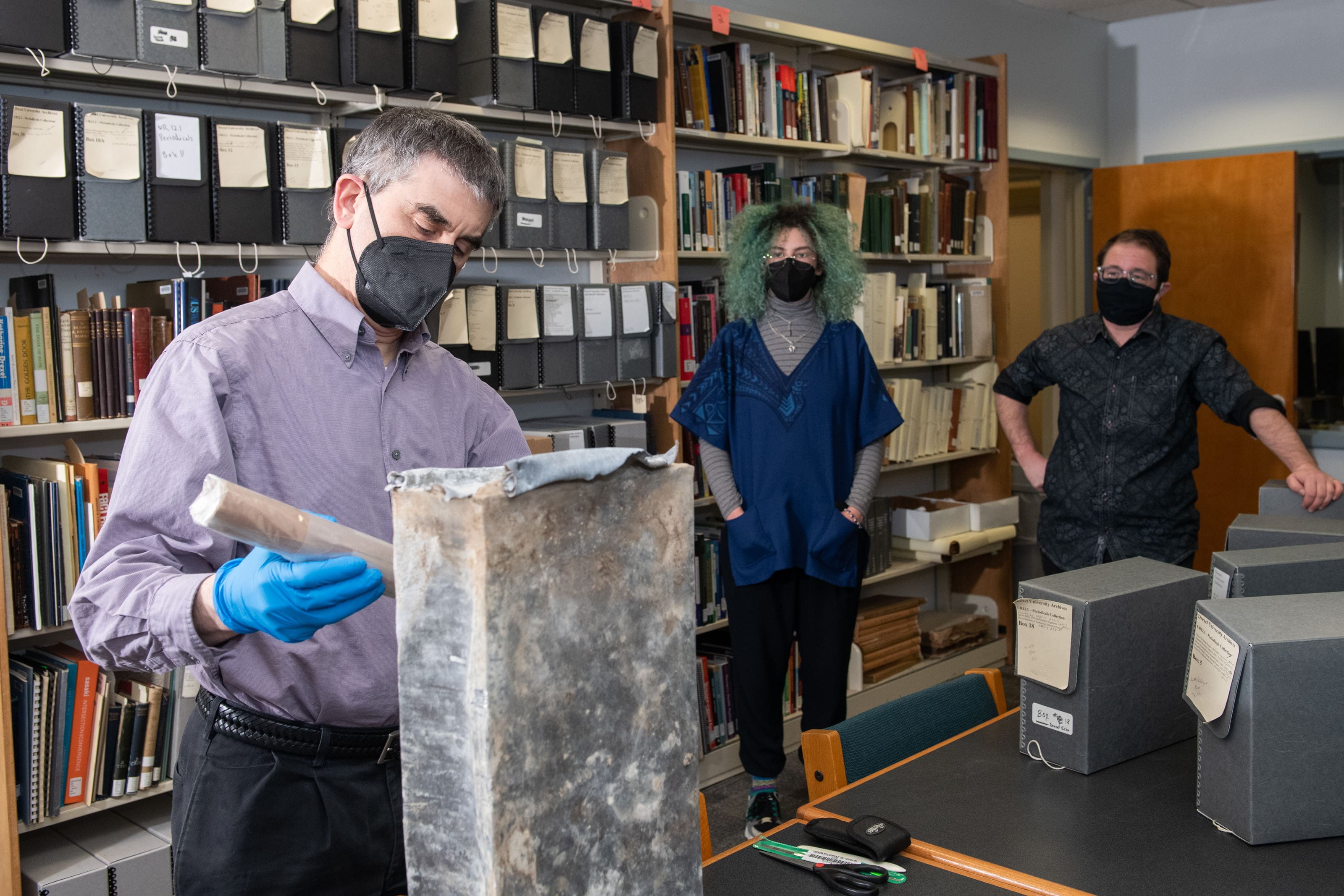 Photo credit: Jaci Downs. University Archives staff open the time capsule. From left to right: Archivist Matthew Lyons, former Archives Co-Op Hanna Pistorius, and Archivist Simon Ragovin