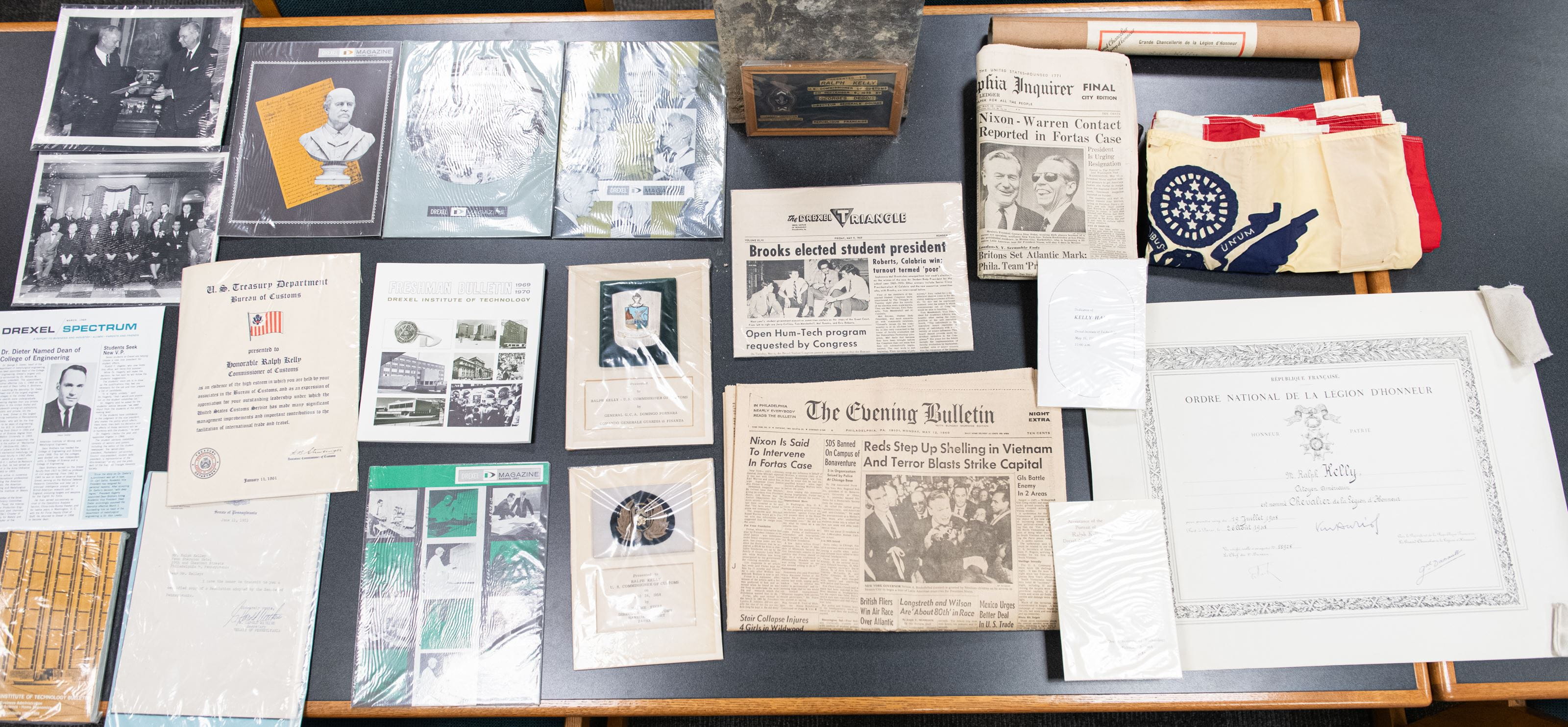 Photo credit: Jaci Downs. Objects from time capsule, including newspapers, Drexel publications, photographs, certificates, and a flag.