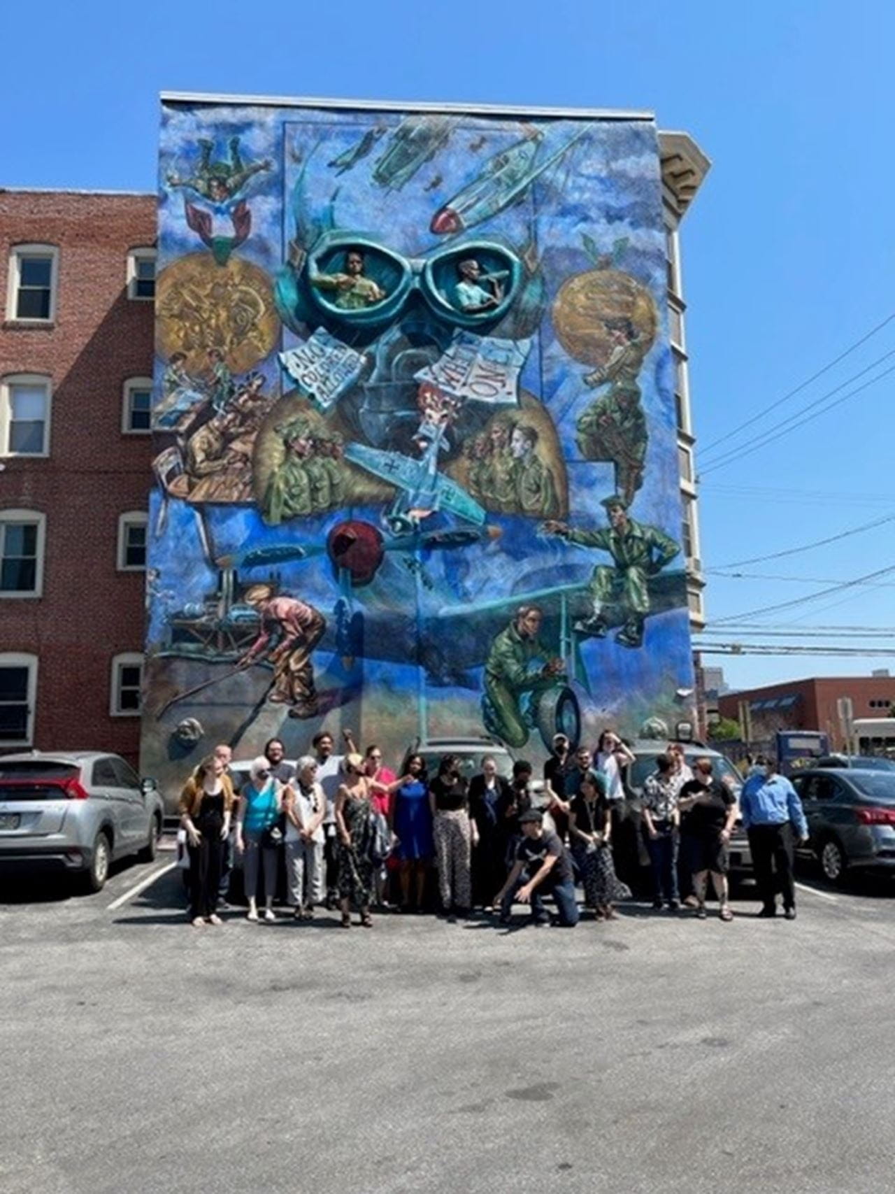 Drexel Libraries staff pose for a group photo in front of the Tuskegee Airmen: They Met the Challenge mural