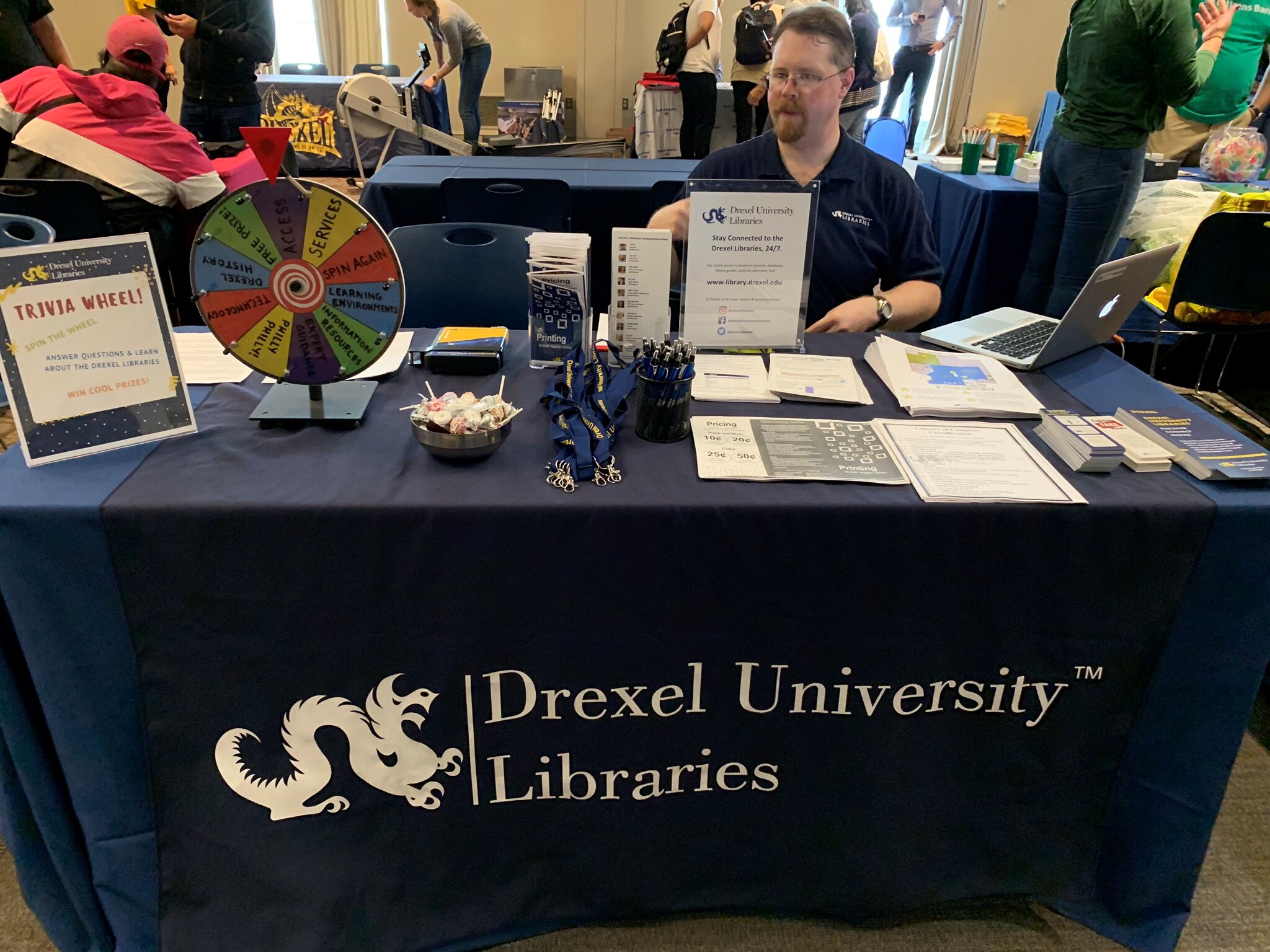 A man sits at a table with brochures and Library swag