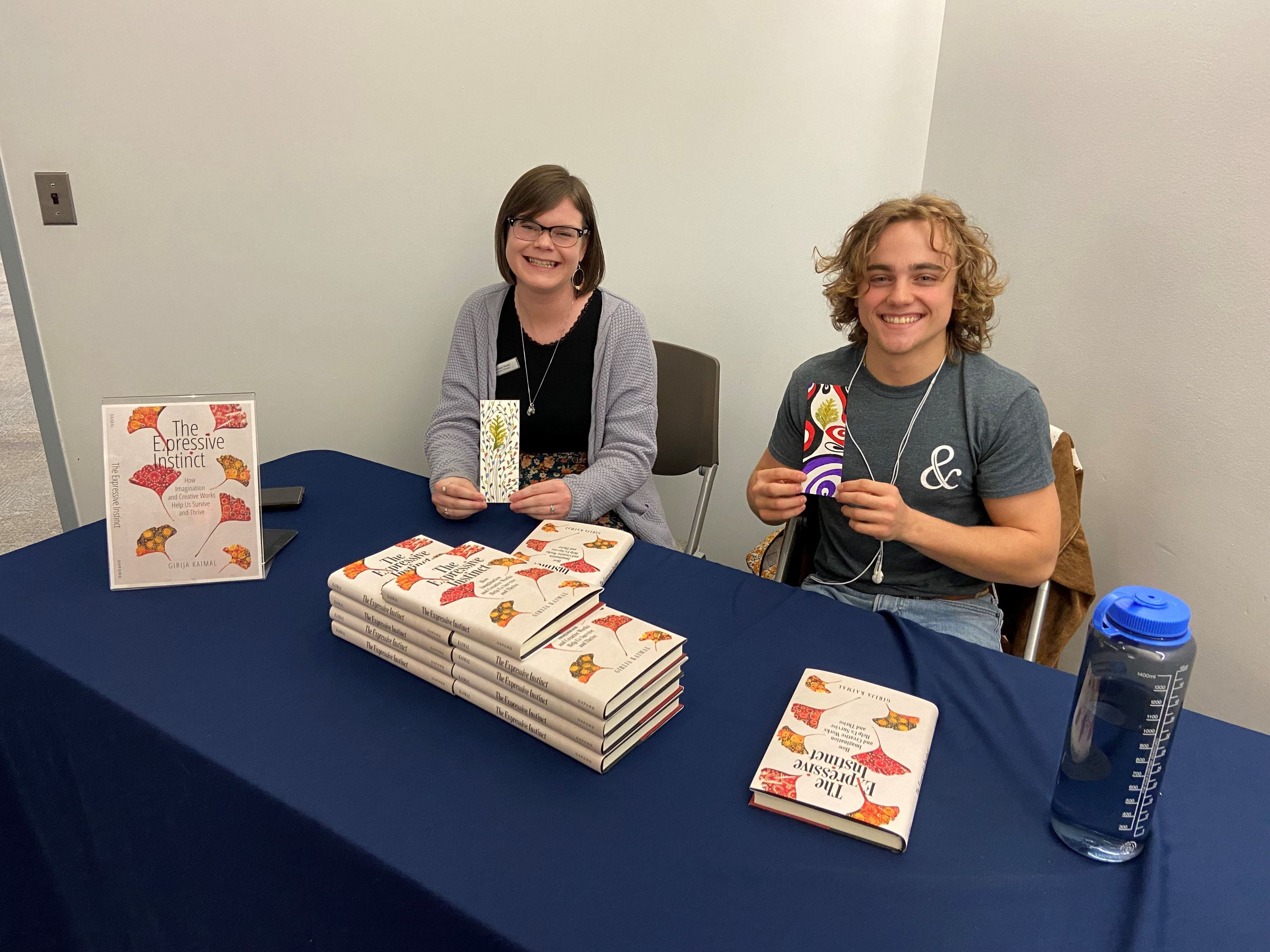Two people holding bookmarks sit at a table with books on it